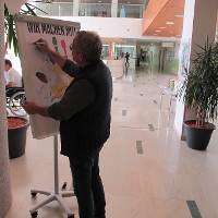 Der Technische Betriebsleiter des Rehabilitationszentrums unterschreibt auf dem Plakat -Wir machen mit!- und zeigt damit, dass auch er das Programm „Aktion Saubere Hände“ unterstützt.