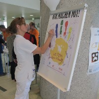 Eine Pflegeperson des Rehabilitationszentrums unterschreibt auf dem Plakat -Wir machen mit!- als Zeichen der Unterstützung des Programms.