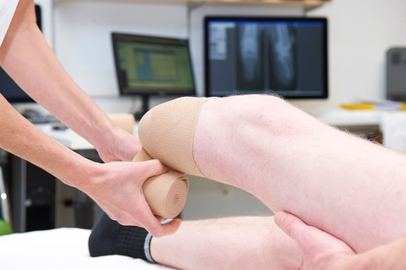 Ein Unterschenkelamputationsstumpf wird mit einer Bandage durch eine Pflegeperson bandagiert.