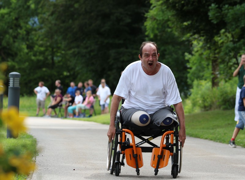 Ein beinamputierter Patient im Rollstuhl fährt so schnell er kann den Weg entlang und wird im Hintergrund von Personen angefeuert.